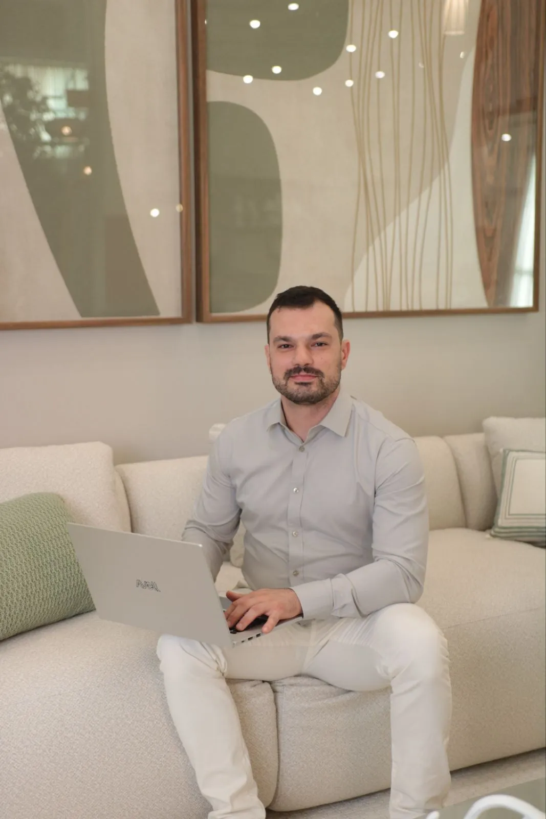 Fillipi Truppel Fernandes sentado num sofá, com o notebook apoiado nas pernas, olhando para a câmera